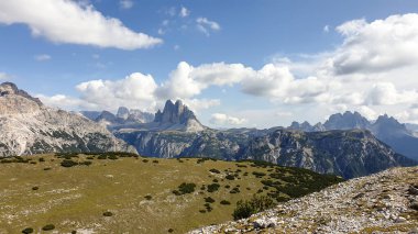 A distant view on Drei Zinnen from Strudelkopf in Italian Dolomites. The famous mountains are surrounded by many massive mountain chains. A lush green meadow in front. High Alpine landscape. Freedom
