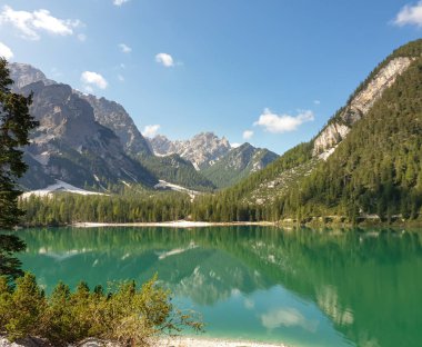 A panoramic view on the Pragser Wildsee, a lake in South Tyrolean Dolomites. High mountain chains around the lake. The sky and mountains are reflecting in the lake. Dense forest at the shore. Serenity