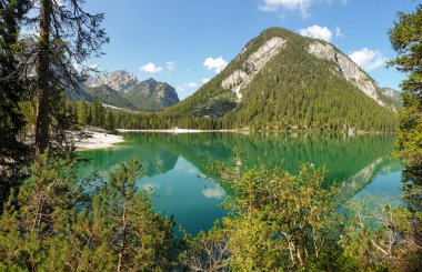A panoramic view on the Pragser Wildsee, a lake in South Tyrolean Dolomites. High mountain chains around the lake. The sky and mountains are reflecting in the lake. Dense forest at the shore. Serenity