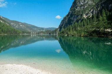 A panoramic view on the Pragser Wildsee, a lake in South Tyrolean Dolomites. High mountain chains around the lake. The sky and mountains are reflecting in the lake. Dense forest at the shore. Serenity