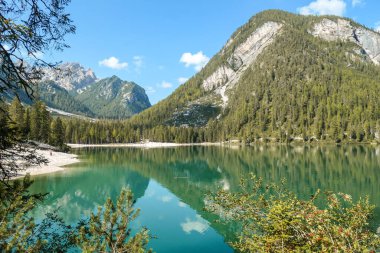 A view on the Pragser Wildsee, a lake in South Tyrolean Dolomites. High mountain chains around the lake. The sky and mountains are reflecting in the lake. Dense forest at the shore. Autumn vibe. Relax
