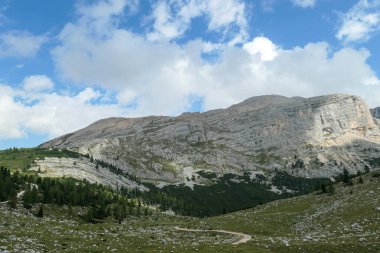 A close up view on a sharp and stony mountain in Italian Dolomites. The massive mountain is surrounded by clouds. There is a green forest at the bottom of the valley. Remote and desolate landscape