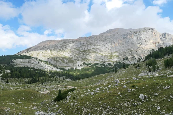 A close up view on a sharp and stony mountain in Italian Dolomites. The massive mountain is surrounded by clouds. There is a green forest at the bottom of the valley. Remote and desolate landscape