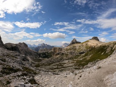 A panoramic view on a high and desolated mountain peaks in Italian Dolomites. The lower parts of the mountains are overgrown with moss and grass. Raw and unspoiled landscape. A bit of overcast.