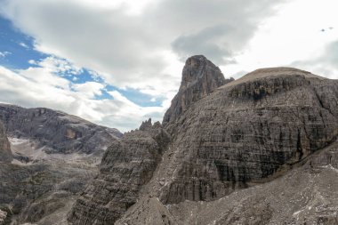 A close up view on a massive, high and desolated mountain wall in Italian Dolomites. The wall has sandy color with some darker shades. Dangerous climbing route. Few green plants on the steep slopes.