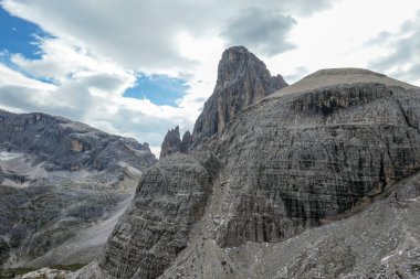 A close up view on a massive, high and desolated mountain wall in Italian Dolomites. The wall has sandy color with some darker shades. Dangerous climbing route. Few green plants on the steep slopes.