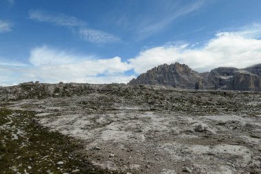 A panoramic view on a high and desolated mountain peaks in Italian Dolomites. The lower parts of the mountains are overgrown with moss and grass. Raw and unspoiled landscape. A bit of overcast.