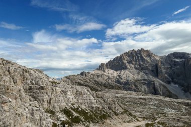 A panoramic view on a high and desolated mountain peaks in Italian Dolomites. The lower parts of the mountains are overgrown with moss and grass. Raw and unspoiled landscape. A bit of overcast.