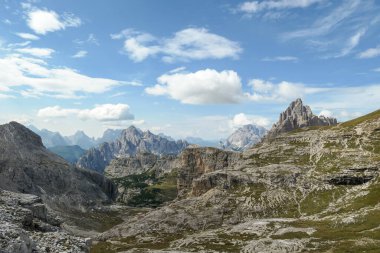 An endless view on a high and desolated mountain peaks in Italian Dolomites. The lower parts of the mountains are overgrown with moss and grass. Raw and unspoiled landscape. Few clouds above the peaks