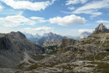An endless view on a high and desolated mountain peaks in Italian Dolomites. The lower parts of the mountains are overgrown with moss and grass. Raw and unspoiled landscape. Few clouds above the peaks