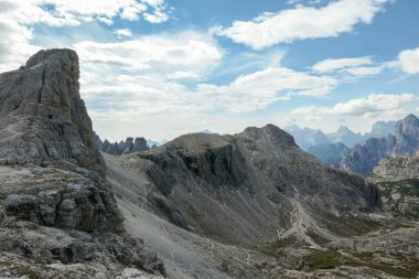 An endless view on a high and desolated mountain peaks in Italian Dolomites. The lower parts of the mountains are overgrown with moss and grass. Raw and unspoiled landscape. Few clouds above the peaks