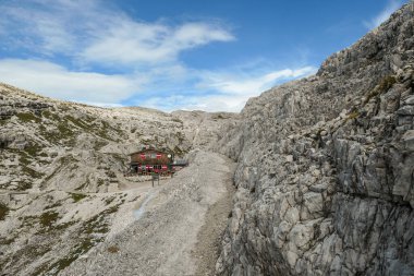 A very narrow and steep pathway, with lots of lose stones in Italian Dolomites. There is a big cottage at the end of it, hidden between the rocks. Raw and unspoiled landscape. Clear and sunny day.