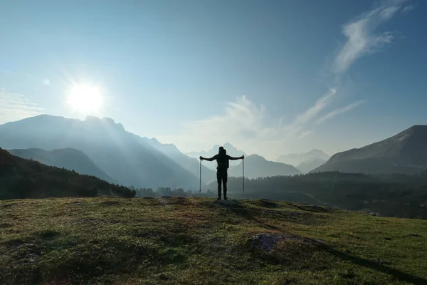 A man with hiking sticks spreading his arms wide open on an early morning in Italian Dolomites. The valley below is shrouded in morning haze. In the back there are high mountain chains. Golden hour