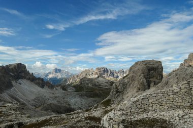 An endless view on a high and desolated mountain peaks in Italian Dolomites. The lower parts of the mountains are overgrown with moss and grass. Raw and unspoiled landscape. Few clouds above the peaks