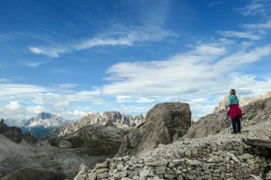 A woman hiking in high and desolated mountains in Italian Dolomites. She stands at the edge of a slope and enjoys the idyllic landscape. Raw and unspoiled landscape. Sunny day. Endless mountain chains