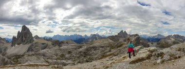 A woman hiking in high and desolated mountains in Italian Dolomites. She walks along the mountain rim and enjoys the idyllic landscape. Raw and unspoiled landscape. Sunny day. Endless mountain chains