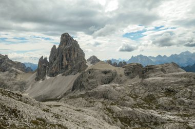 A panoramic view on a valley in Italian Dolomites. There is a massive mountain in front, with very steep and sharp slopes. In the back there are smaller mountain chains. Raw and desolated landscape