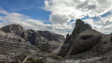 A panoramic view on Italian Dolomites. There are many high and sharp peak in front, with many landslides. Dangerous climbing. Barely any plants growing in the  area. Raw and unspoiled landscape.