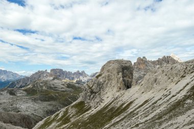 A panoramic view on a valley in Italian Dolomites. There is a massive mountain in front, with very steep and sharp slopes. In the back there are smaller mountain chains. Raw and desolated landscape