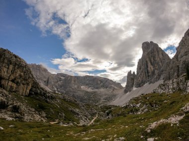 Panoramic view on the valley in Italian Dolomites. The bottom of the valley is overgrown with small plants. In the back there is a high mountain chain, with very sharp slopes. Serenity and recharging