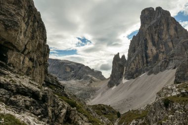 A panoramic view on Italian Dolomites. There are many high and sharp peak in front, with many landslides. Dangerous climbing. Barely any plants growing in the  area. Raw and unspoiled landscape.