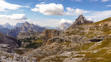 A panoramic view on a high and desolated mountain peaks in Italian Dolomites. The lower parts of the mountains are overgrown with moss and grass. Raw and unspoiled landscape. A bit of overcast.