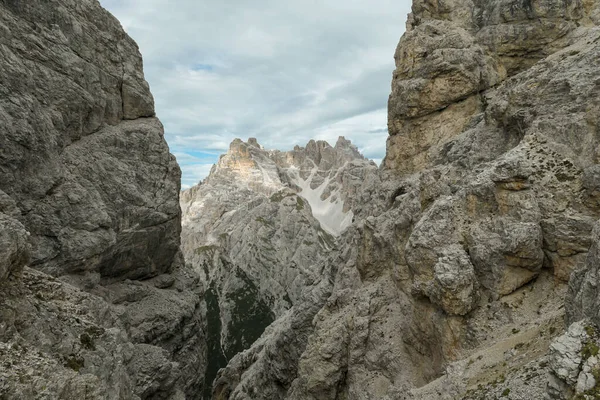 A sneak-peak on a high and distant mountain in Italian Dolomites. The mountain is visible between two rocky and steep slopes in front. Playing hide and seek. Raw and desolate landscape. Overcast