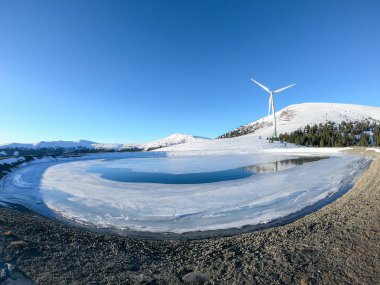 An early, wintery morning in the region of Stubalpe, Austria. The whole area is covered with powder snow. There is an artificial lake, covered with thin layer of ice and a windmill next to it. Sunny clipart