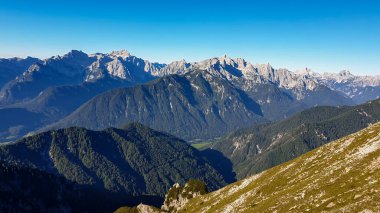 Panoramic view on the haze shrouded valley from the way to Mittagskogel in Austrian Alps. Clear and sunny day. Endless mountain chains. Outdoor activity. Barren top of the mountains, lush lower parts