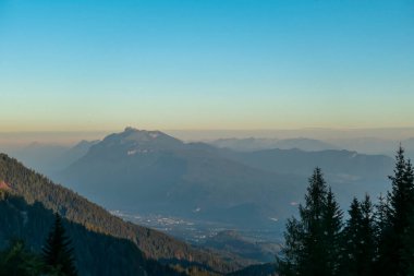 A panoramic view on the haze shrouded valley from the way to Mittagskogel in Austrian Alps. The horizon line is orange. Clear and sunny day. Endless mountain chains. Outdoor activity. Daybreak