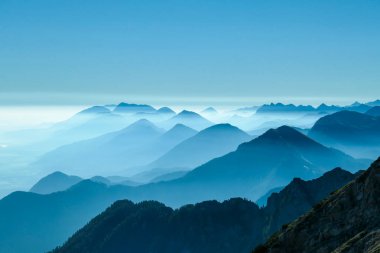 A close up view on the Alpine chains shrouded in the morning fog, seen from the top of Mittagskogel in Austria. Clear and sunny day. Sharp peaks around. Sun is shining above the high peaks. Serenity