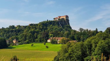 Riegersburg castle in Austria towering above the area. There are mais crops ripening on the field in front. Clear blue sky above the castle. The massive fortress was build on the rock. Middle ages