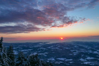 A sunrise seen from snow-capped peak of Schoeckl in Austrian Alps. The sky is bursting with orange and pink. Distant view on Graz, shrouded with fog. Winter wonderland. Day break. Calmness