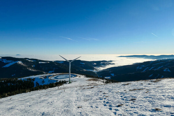 An early, wintery morning in the region of Stubalpe, Austria. The whole area is covered with powder snow. There is an artificial lake, covered with thin layer of ice and a windmill next to it. Sunny