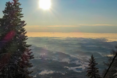 A sunrise seen from snow-capped peak of Schoeckl in Austrian Alps. The sky is bursting with orange and pink. Distant view on Graz, shrouded with fog. Winter wonderland. Day break. Calmness