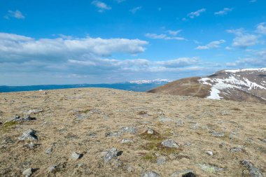 A panoramic view on an Alpine chain in Austria. The vast pasture has golden colors. There are other mountain chains in the back. A narrow pathway leading to the top. Overcast. Serenity and calmness