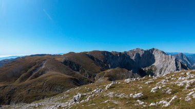 A panoramic view on Hochschwab mountain chains from the pathway leading to Hohe Weichsel. There is a vast pasture on top of a mountain, slowly turning golden. Clear view. Blue sky above. Autumn vibe