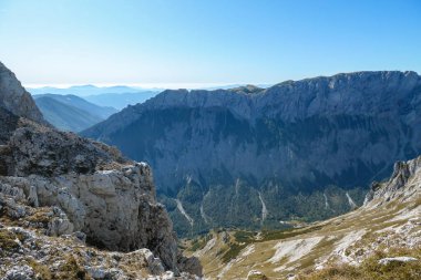 A panoramic view on Hochschwab mountain chains from the pathway leading to Hohe Weichsel. Sharp mountain slopes. Endless mountain chains, some shrouded with haze. Clear view. Blue sky above.