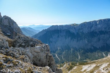 A panoramic view on Hochschwab mountain chains from the pathway leading to Hohe Weichsel. Sharp mountain slopes. Endless mountain chains, some shrouded with haze. Clear view. Blue sky above.