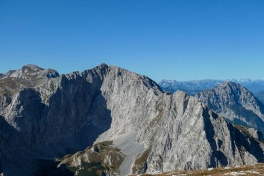 A panoramic view on Hochschwab mountain chains from the pathway leading to Hohe Weichsel. Sharp mountain slopes. Endless mountain chains, some shrouded with haze. Clear view. Blue sky above.