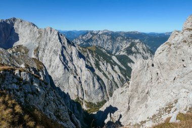 A panoramic view on Hochschwab mountain chains from the pathway leading to Hohe Weichsel. Sharp mountain slopes. Endless mountain chains, some shrouded with haze. Clear view. Blue sky above.