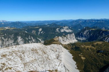 A panoramic view on Hochschwab mountain chains from the pathway leading to Hohe Weichsel. Sharp mountain slopes. Endless mountain chains, some shrouded with haze. Clear view. Blue sky above.