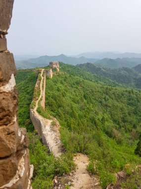 A panoramic view on an unrenewed Gubeikou part of Great Wall of China. The wall is spreading on tops of mountains. Many watchtowers on the peaks. Dense forest around it. World wonder. Tradition