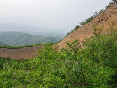 A panoramic view on an unrenewed Gubeikou part of Great Wall of China. The wall is spreading on tops of mountains. Many watchtowers on the peaks. Dense forest around it. World wonder. Tradition