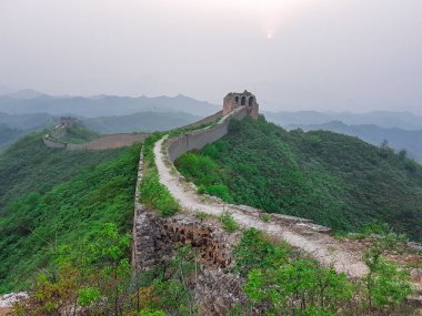 A panoramic view on an unrenewed Gubeikou part of Great Wall of China. The wall is spreading on tops of mountains. Many watchtowers on the peaks. Dense forest around it. World wonder. Tradition
