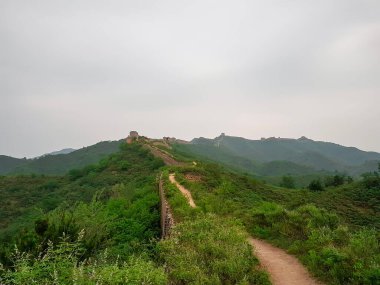 A panoramic view on an unrenewed Gubeikou part of Great Wall of China. The wall is spreading on tops of mountains. Many watchtowers on the peaks. Dense forest around it. World wonder. Tradition