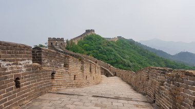 A panoramic view on a renewed Jinshanling part of Great Wall of China. The wall is spreading on tops of mountains. Many watchtowers on the peaks. Dense forest around it. World wonder. Tradition