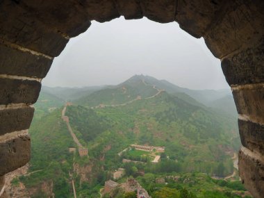 A panoramic view on an unrenewed Gubeikou part of Great Wall of China. The wall is spreading on tops of mountains. Many watchtowers on the peaks. Dense forest around it. World wonder. Tradition