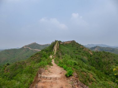 A panoramic view on an unrenewed Gubeikou part of Great Wall of China. The wall is spreading on tops of mountains. Many watchtowers on the peaks. Dense forest around it. World wonder. Tradition