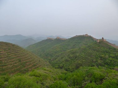 A panoramic view on an unrenewed Gubeikou part of Great Wall of China. The wall is spreading on tops of mountains. Many watchtowers on the peaks. Dense forest around it. World wonder. Tradition